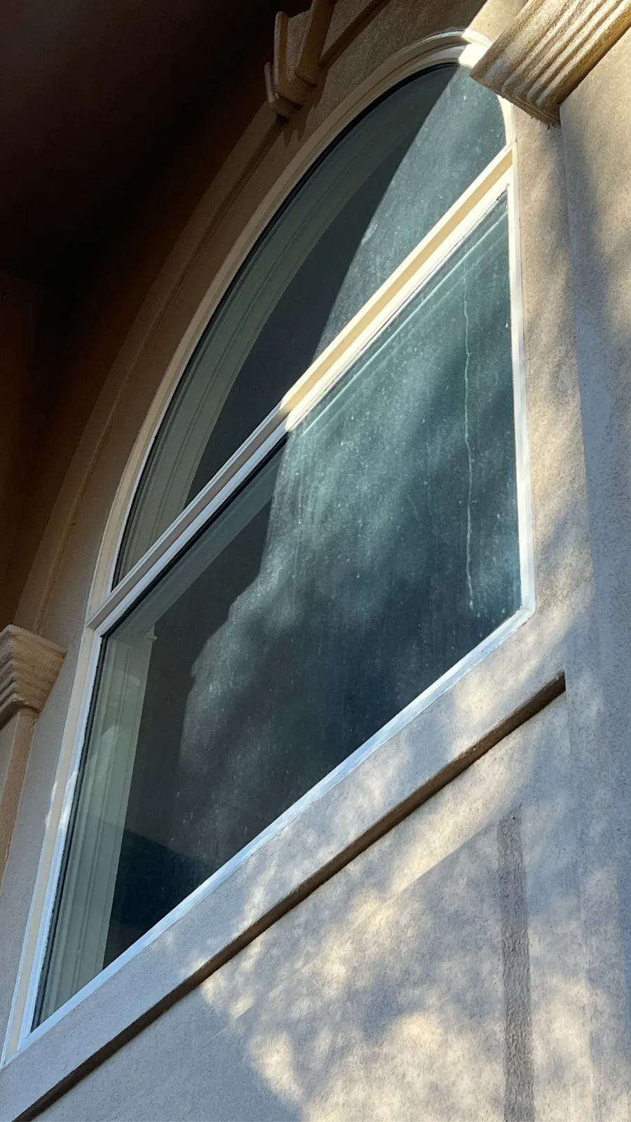 A tall arched stucco window in raking sunlight, showing the dust and water spots that a cleaning visit will remove