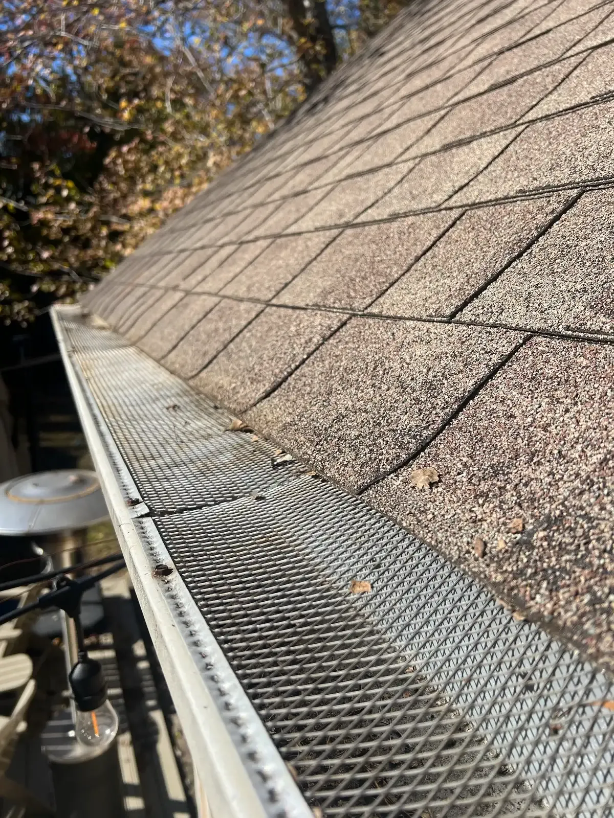 A freshly cleaned aluminum gutter with mesh leaf guard running along the eave of a shingled roof