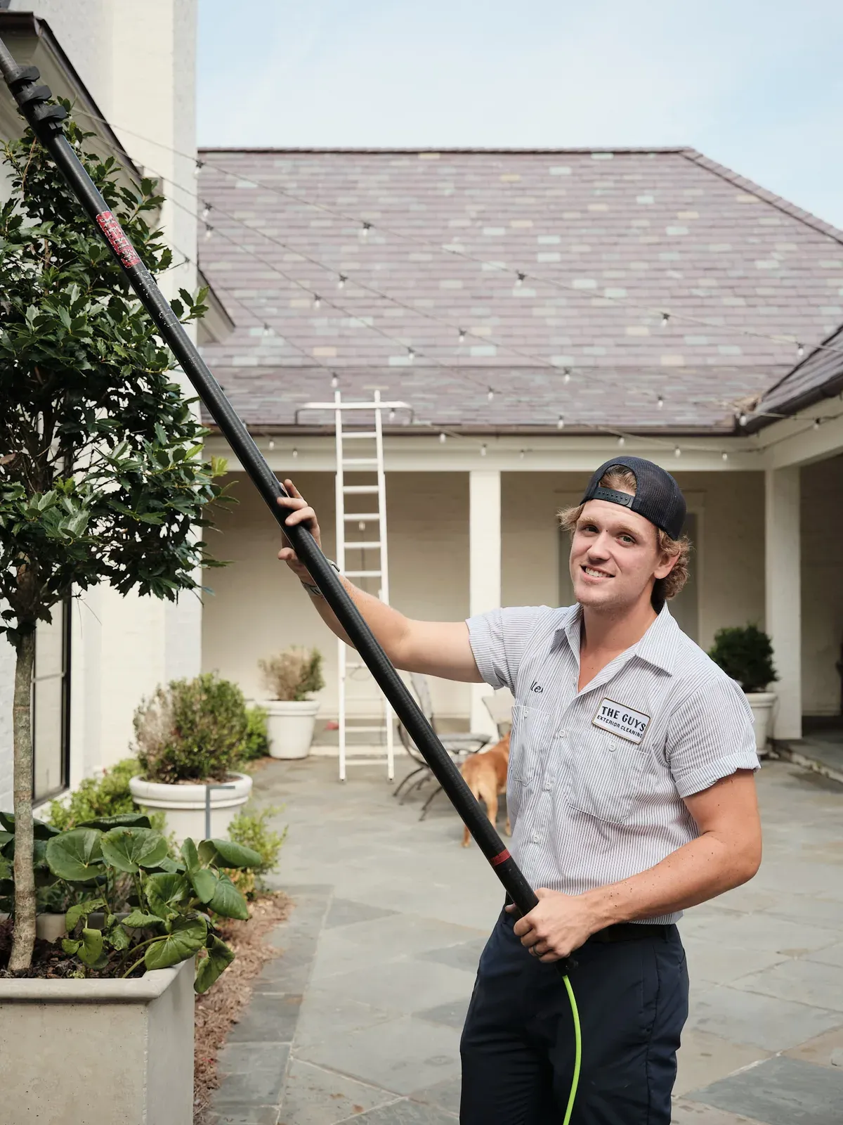 The Guys Exterior Cleaning technician soft-washing a home with an extension pole beside a set ladder in Madison, MS